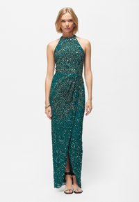 Abito da sera turchese con paillettes, dotato di scollo all'americana, complesso lavoro di perline e uno spacco frontale. Presenta un tessuto liscio e un design aderente.