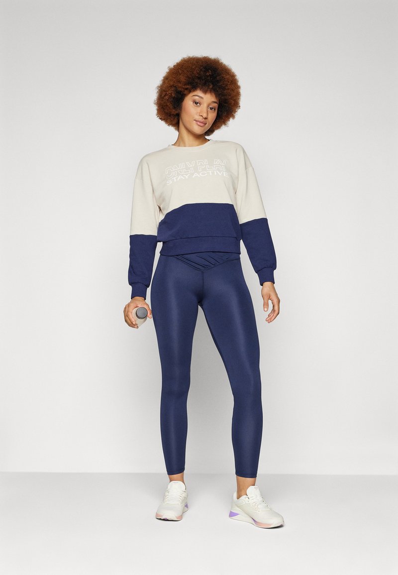 Granatowe legginsy z wysokim stanem, zestawione z beżowym i granatowym swetrem w kolorowe bloki z białym napisem, wykonanym z mieszanki bawełny i z prążkowanymi mankietami.