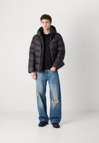 Czarna puchowa kurtka z kapturem, pikowanym wzorem i zamkiem błyskawicznym. Połączona z podniszczonymi jasnoniebieskimi dżinsami i czarnymi butami.