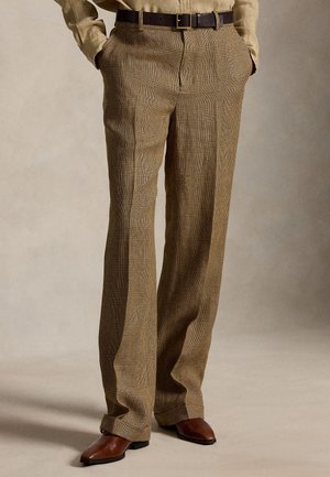 Pantalon à carreaux marron avec pli devant, associé à une ceinture en cuir marron et des chaussures pointues assorties sur fond neutre.