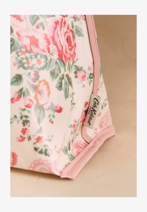 Kukkakuvioinen kangaspussi, jonka kulmassa vaaleanpunainen reunus ja näkyvissä oleva Cath Kidston London -etiketti, vaaleanbeigellä pinnalla.