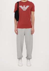 Czerwona koszulka z krótkim rękawem z białym logo, szare dresy i białe tenisówki. Czarna torba przewieszona przez ramię.