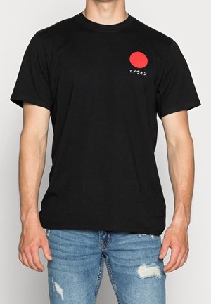 T-shirt en coton noir avec un motif circulaire rouge et du texte japonais sur le côté gauche de la poitrine. Col rond et manches courtes.