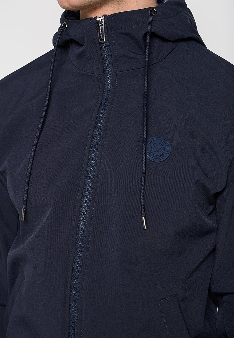 Giacca zip-up blu navy realizzata in tessuto testurizzato, con cappuccio, lacci e una toppa rotonda con logo sul petto. Chiusura a zip in argento.