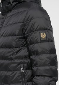 Black quilted puffer jacket with visible zipper pocket and Belstaff logo patch on the upper arm, worn by a person.