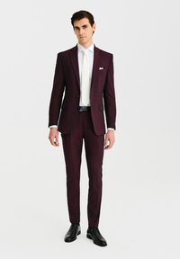 Burgundowa marynarka o dopasowanym kroju, z klapami w ząbkowanej formie, biała koszula i krawat. Czarne skórzane buty oraz subtelny detal w postaci chusteczki w kieszeni.