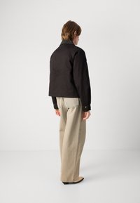 Jachetă neagră scurtă cu mâneci lungi și guler khaki, asociată cu pantaloni bej cu picioare largi. Design simplu cu accente de nasturi aurii.
