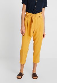 Gula, högmidjade, korta byxor med knytbälte och sidofickor. Bärs med en navy-blå topp och bruna vävda sandaler. Slät tyg.