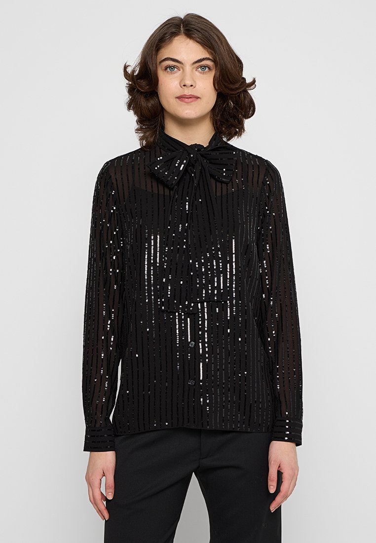 Zwarte doorschijnende blouse met een strik-kraag, voorzien van verticale paillettenstrepen en lange mouwen. Voorzien van knoopsluiting aan de voorkant en een aansluitende pasvorm.