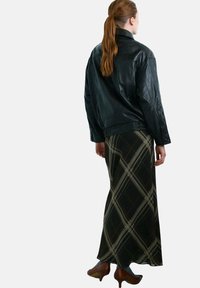 Chaqueta de cuero negra de ajuste relajado, combinada con una falda larga a cuadros en tonos verdes, crema y marrón, usada con zapatos de tacón marrones.