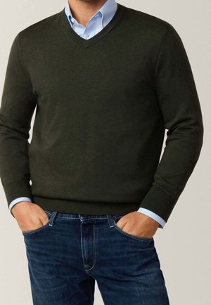 Dunkelgrüner V-Ausschnitt-Pullover aus einem glatten Strickmaterial; getragen über einem hellblauen Hemd mit Kragen und Jeans. Einfache Bündchen und Design.