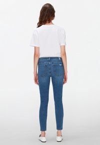 Jeans ajustados en denim azul medio, con una cintura de media altura, bolsillos traseros y una textura suave. Combinados con una camiseta blanca lisa.