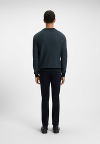Dark blue knitted sweater with a round neckline and ribbed cuffs, paired with black slim-fit pants and black shoes. Worn from the back.