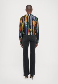 Camicia a maniche lunghe in tessuto nero con motivi colorati che somigliano a graffette, abbinata a jeans neri aderenti e scarpe con tacco.