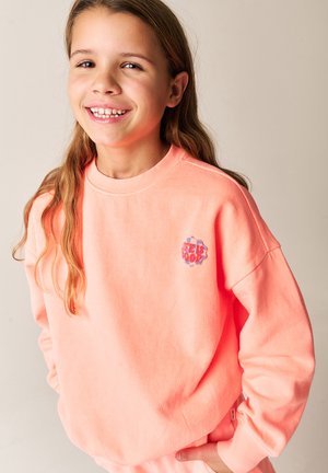 Lys koralfarvet sweatshirt med en blød tekstur, rund halsudskæring og et broderet mærke med teksten "FEELS GOOD" på brystet. Lange ærmer.