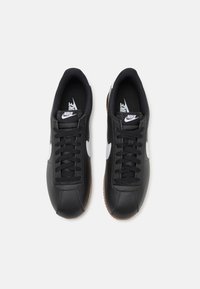 Nike sneakers in black leather with white accents. Features include black laces, textured black inner lining, and a gum rubber outsole.
