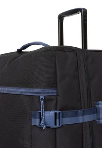 Valigia di tessuto nera con manico retrattile, accenti blu, tracolla laterale, dettagli con zip e una robusta fibbia per una chiusura sicura.