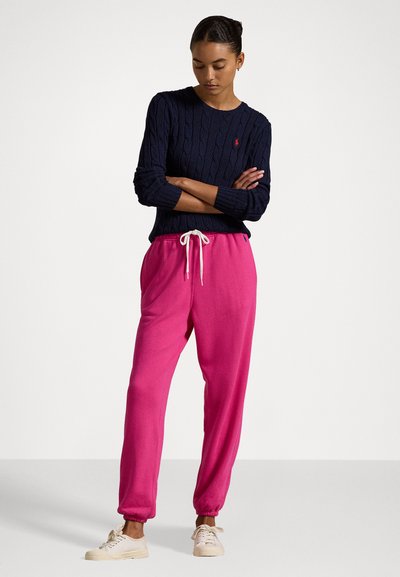 Marinblå kabelstickad tröja i kombination med ljusrosa sweatpants med elastiska manschetter och snörning. Casual vita sneakers fulländar looken.