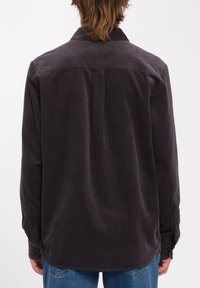 Chemise en velours côtelé gris foncé avec des manches longues, des poignets boutonnés et un détail de couture au dos. Texture douce avec un design de col classique.