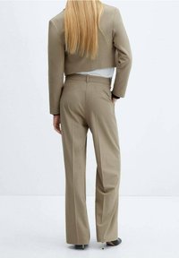 Blazer beige cropped avec un pantalon tailleur assorti. Tissu lisse, coupe droite et coutures discrètes. Accents noirs sur les poignets du blazer.