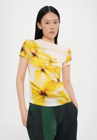 Kremfarget topp med korte ermer og et gult blomstermønster, med innsamlet detaljering på siden og et mykt, lett stoff.