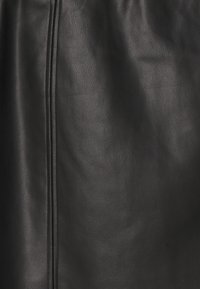 Material de cuero negro con una superficie suave y ligeramente texturada. Presenta una costura central que corre verticalmente, destacando el diseño de la prenda.