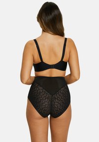 Conjunto de lencería negra que incluye un sujetador liso y bragas de cintura alta con una espalda de malla intrincadamente decorada con un patrón de hojas, tirantes ajustables y cierre de gancho.