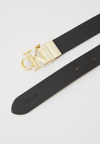 Schwarzer Leder Gürtel mit strukturierter Oberfläche, ausgestattet mit einer goldenen Metall Schnalle mit eingeprägtem "CK"-Logo und verstellbaren Löchern entlang des Riemens.