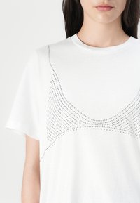 White cotton t-shirt featuring a dotted design in silver along the upper front. Classic crew neck and short sleeves complete the style.