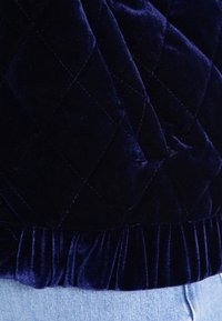 Tessuto in velluto trapuntato blu navy con orlo arricciato. La texture è soffice, caratterizzata da un motivo a diamante e una finitura liscia.