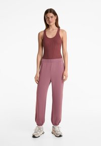 Ribbet bordeaux tanktop parret med pink joggingbukser med elastisk talje og opsmøgede ankler, komplementeret af beige sneakers.