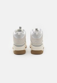 Weiße und graue Sportschuhe mit einer strukturierten Wildleder-Oberfläche, gepolstertem Schaft und brauner Gummisohle. Verfügen über ein Logo und eine Fersenzuglasche.