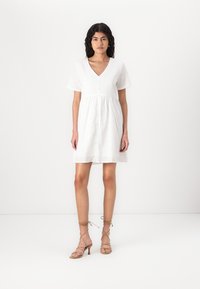 Bílé bavlněné šaty s výst�řihem do V a krátkými rukávy, zdobené výšivkou s dírkováním a zapínáním na knoflíky vpředu. A-liniový střih a lehká textura.