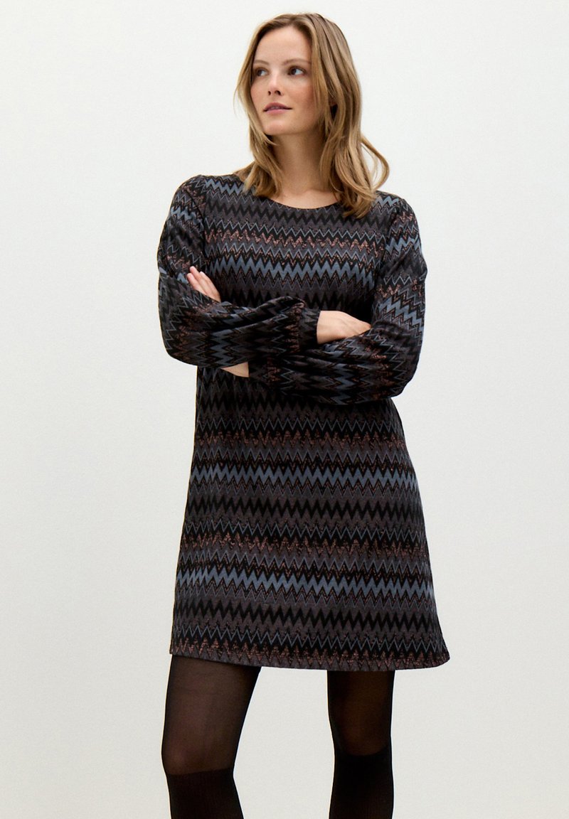 Langärmliges Strickkleid mit einem Zickzackmuster in dunklen Farbtönen und Bronzeakzenten. Weiche Textur, lockere Passform und knielange Gestaltung.