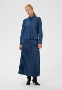 Farmereing gallérrel és elülső zsebbel, hosszú, mélykék rakott szoknyával párosítva. Fekete, térd fölé érő csizmák egészítik ki az öltözéket.