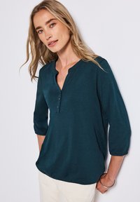 Chemise teal à manches trois-quarts avec un col henley, dotée de trois boutons et d'une texture lisse et légère. Coupe décontractée.