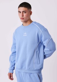 Lichtblauwe sweatshirt gemaakt van zachte stof, met witte piping accenten, een ronde hals en een logo op de borst. Inclusief zijzakdetail.