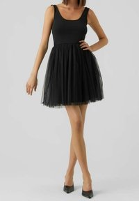 Schwarzes Kleid mit figurbetontem Oberteil und Tüllrock, mit Rundhalsausschnitt und ärmellosem Design, kombiniert mit schwarzen spitzen Schuhen.