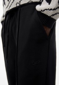 Person wearing black pants with side pockets and a black-and-white patterned sweater, hand partially in pocket.