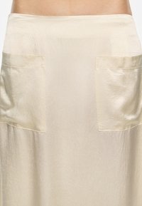 Une jupe de couleur crème avec une finition texturée, dotée de deux poches à rabat à l'avant et d'une taille lisse.
