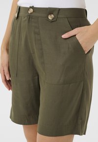 Szorty w kolorze oliwkowej zieleni wykonane z tkaniny plecionej, posiadają dwie przednie kieszenie, dwa guziki w talii oraz dopasowany krój z prostą linią.