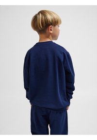 Felpa blu navy con maniche lunghe, collo a giro e vestibilità rilassata, realizzata in tessuto morbido; indossata con pantaloni coordinati.