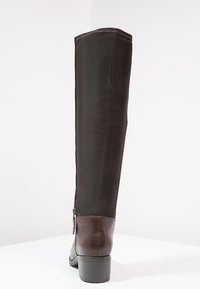 Bota de caña alta con sección inferior de cuero marrón y parte superior de textil negro, con cremallera lateral y tacón apilado. Textura suave.