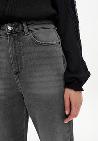 Šedé džíny z denimu s vysokým pasem, s klasickým pětiokrovým stylem, jemným vyblednutím a slim fit střihem, zkombinované s černou texturovanou blůzou.