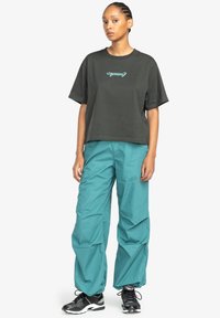 Black cotton t-shirt with turquoise graphic design, paired with loose-fitting teal pants. Black athletic sneakers with textured accents.