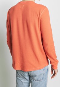 T-shirt à manches longues en maille, de couleur orange vif, avec un col rond et des poignets ajustés, associé à un jean en denim bleu clair.