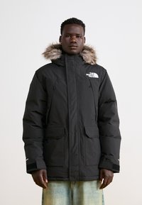 Melnā pūkainā jaka ar vilnas oderi kapuci, ar rāvējslēdzēju, divām priekšējām kabatām un North Face logo uz krūts.