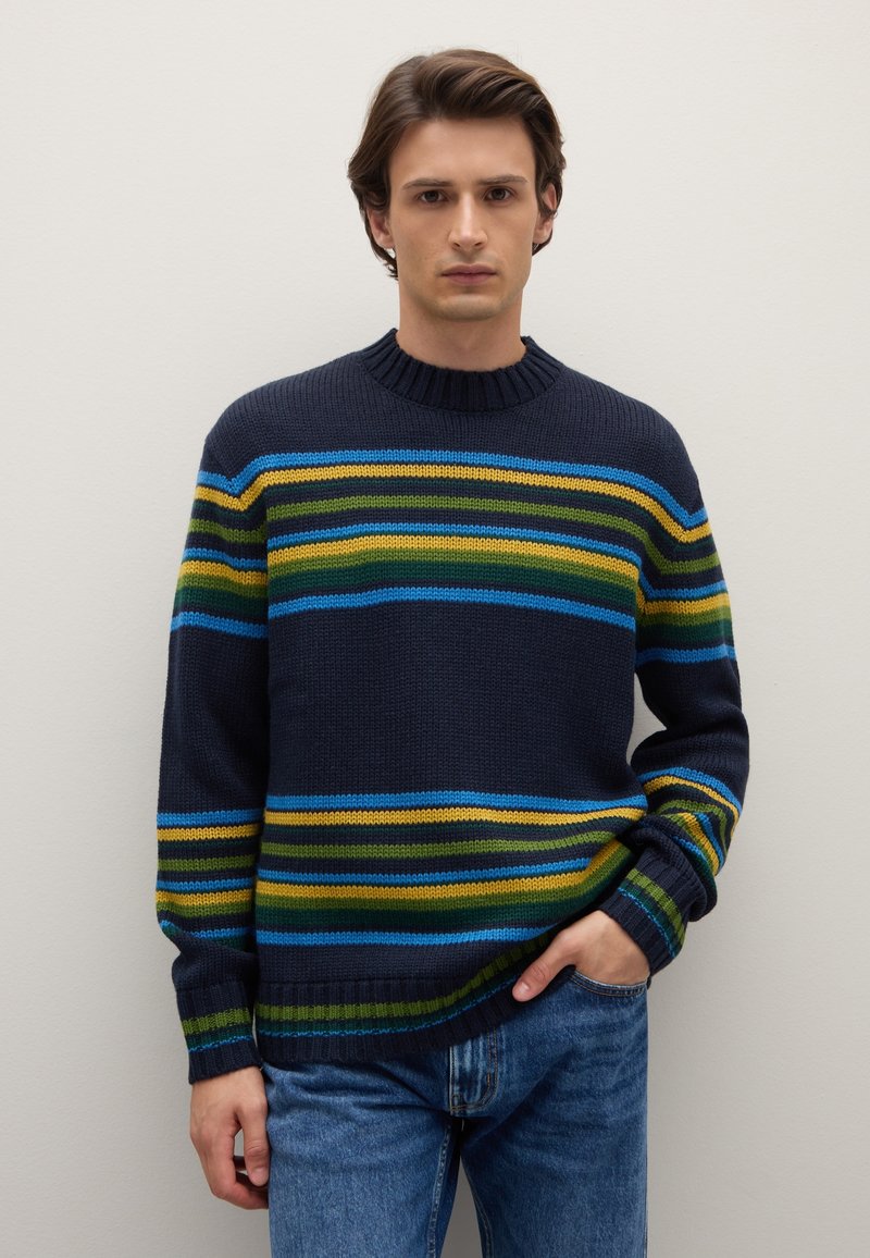 Marineblauer Strickpullover mit horizontalen Streifen in Blau, Grün und Gelb. Verfügt über einen gerippten Kragen und Bündchen. Kombiniert mit blauen Jeans aus Denim.