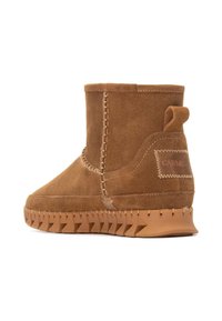 Botín de ante marrón con detalles de costura, suela de goma texturizada y un pequeño lazo en la parte trasera para facilitar su uso. Marca CARMEL en el lateral.