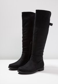 Czarne kozaki do kolan wykonane z miękkiego zamszu, z bocznym zamkiem błyskawicznym i niską gumową podeszwą. Gładka faktura z lekko spiczastym noskiem.